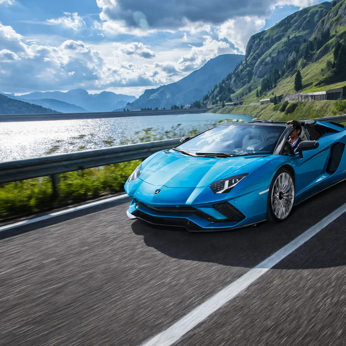 Blauwe Lamborghini Aventador Roadster op een bergweg langs een meer